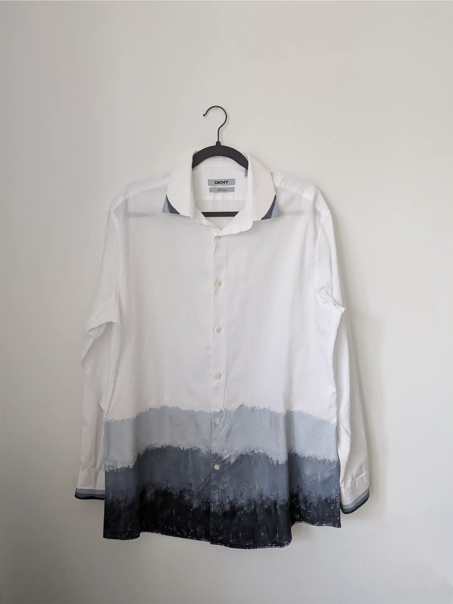 White shirt with gradient design on a hanger against a plain background