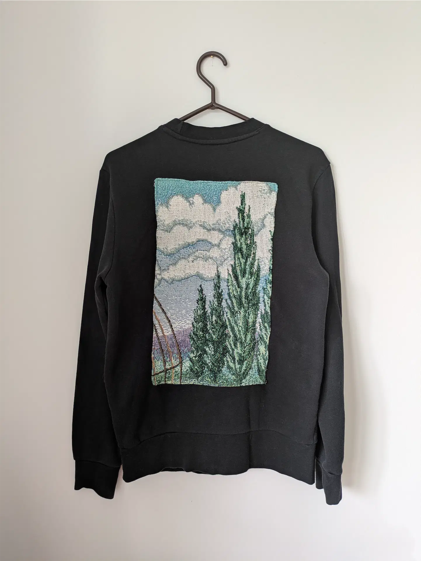 Black sweatshirt with a nature-themed graphic on a hanger against a white background