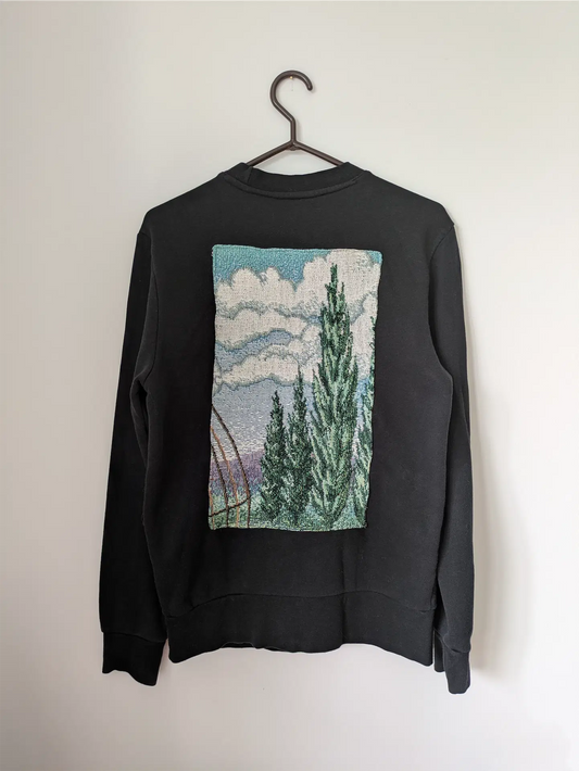 Black sweatshirt with a nature-themed graphic on a hanger against a white background