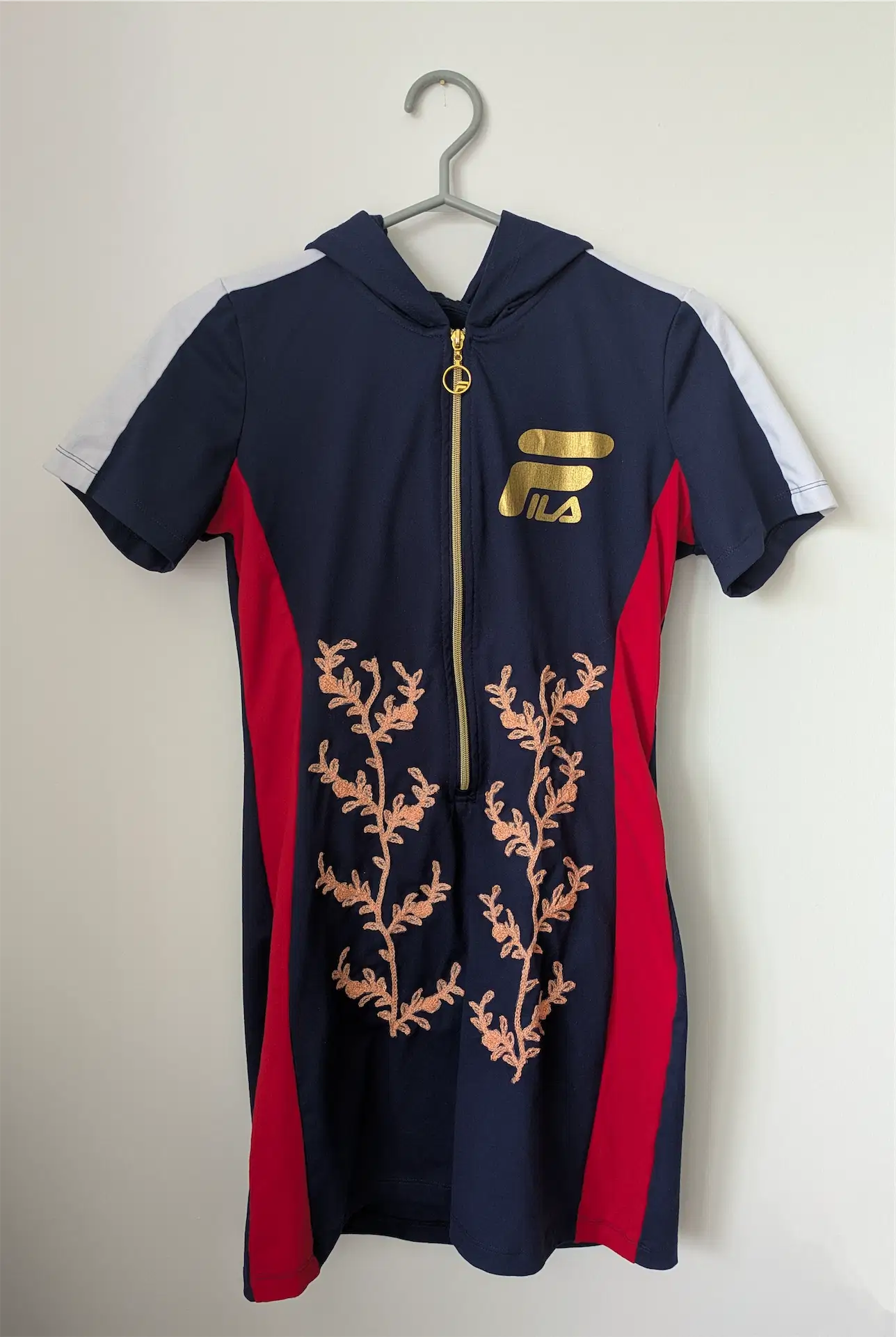 Navy and red dress with floral design and gold zipper on a hanger against a white background