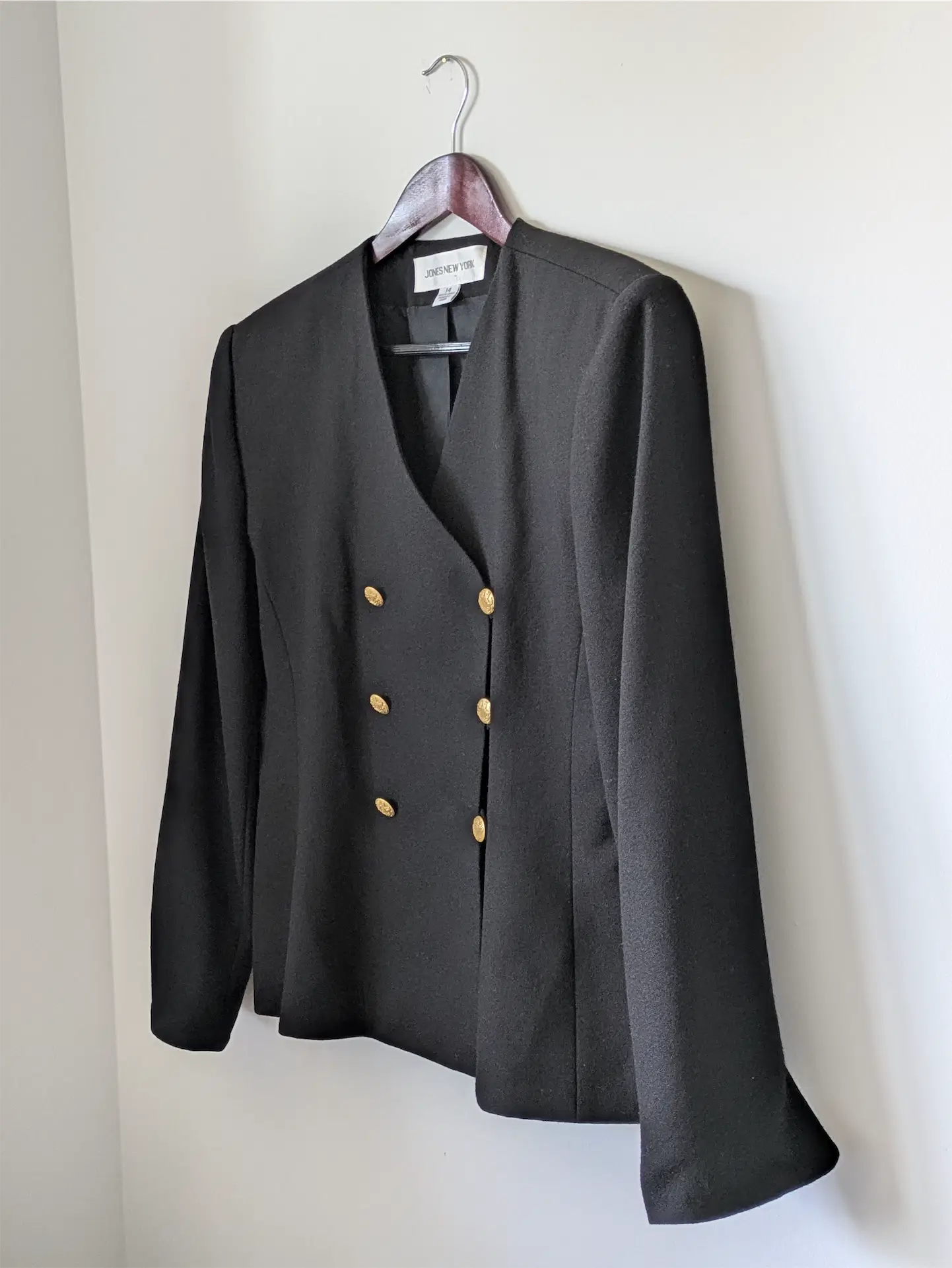 Black blazer with gold buttons on a hanger against a white background