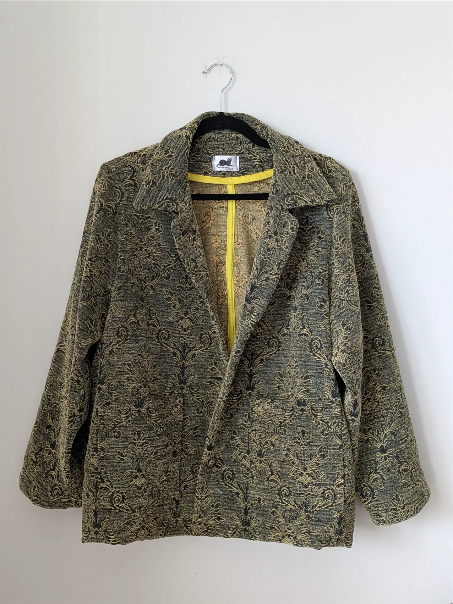 Green patterned jacket on a hanger against a white background