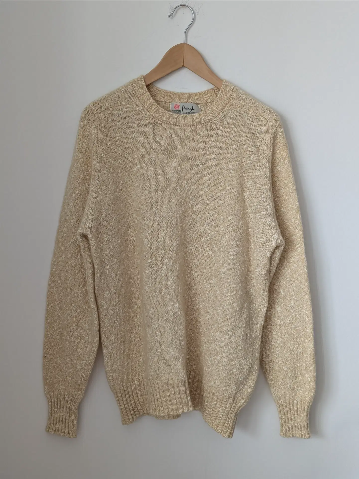 Beige sweater on a wooden hanger against a plain background